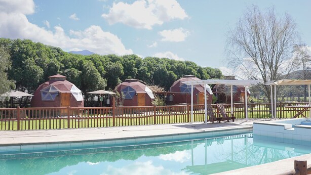 A pool area with three dome-shaped cabins, a wooden fence, and a clear sky. - DOmos Ocoa (Hijuelas)