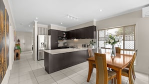 A modern kitchen with dark cabinets, a central island, and a dining area with a wooden table and chairs. - "Poolside Escape in Scarborough" (Scarborough)