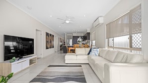 A modern living room with a flat-screen TV, a white sofa, a patterned rug, and a ceiling fan. - "Poolside Escape in Scarborough" (Scarborough)
