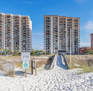 Ein Apartmentkomplex direkt am Strand mit mehreren Hochhäusern, blauem Himmel und einem Sandweg zum Strand.