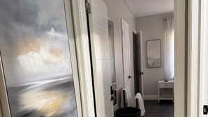 A hallway with a large abstract painting, a white door, a white bench, and a black trash bin.