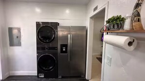 A compact kitchen with a built-in washer and dryer, a wooden shelf with plants, and a roll of paper towels.