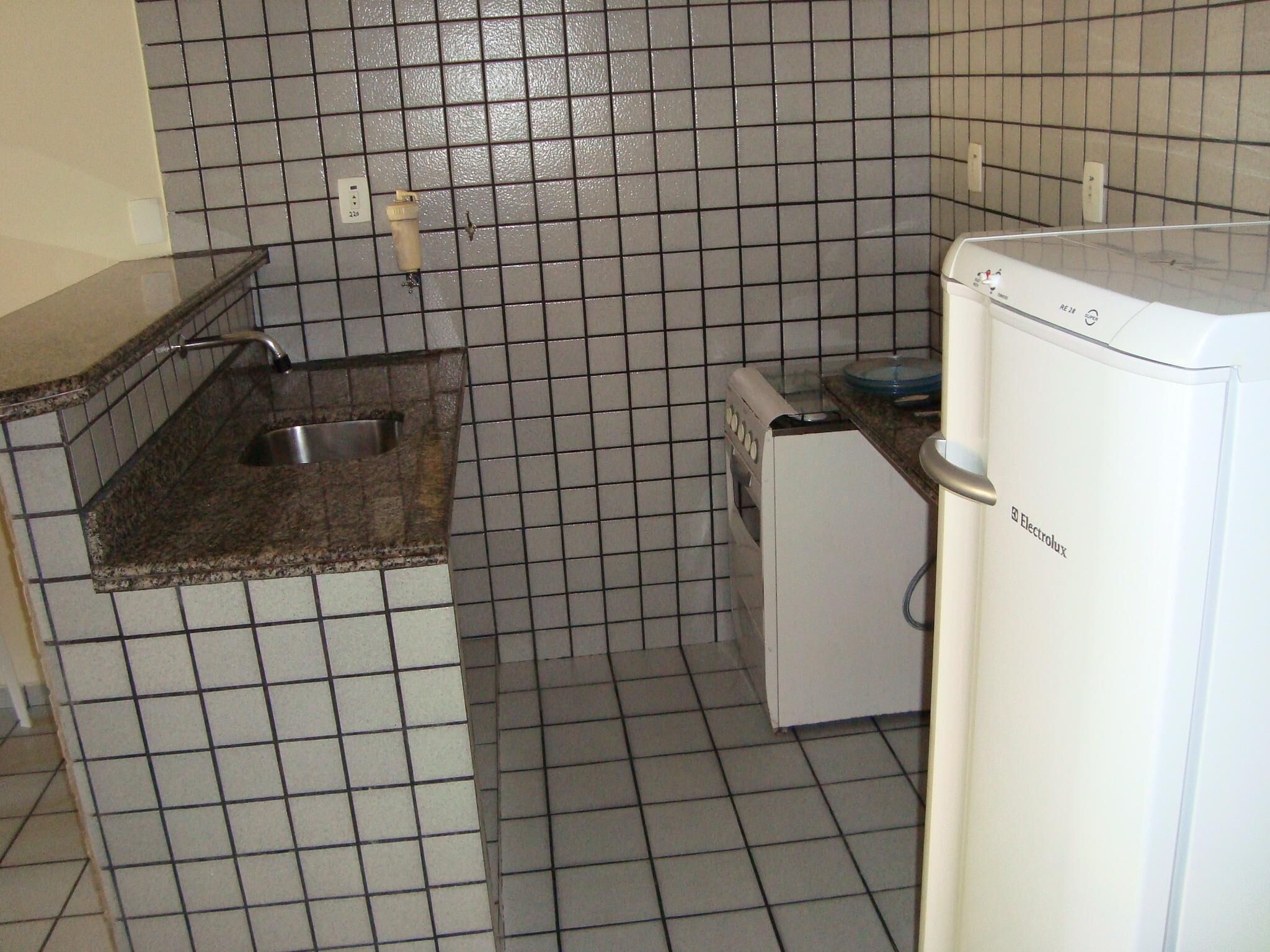 A compact kitchen with a sink, a small refrigerator, and tiled walls.