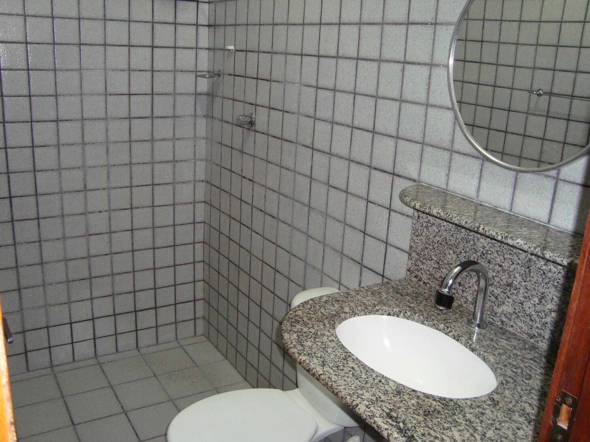 Et badeværelse med et hvidt toilet, en granitvask og et spejl over vasken.