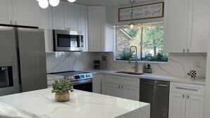 A modern kitchen with white cabinetry, a marble island, stainless steel appliances, and a pendant light. - The Woodlands Retreat Getaway & Theater Luxury (The Woodlands)