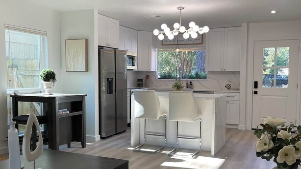A modern kitchen with white cabinets, a dining area with a table and chairs, a ceiling fan, and a hanging light fixture. - The Woodlands Retreat Getaway & Theater Luxury (The Woodlands)