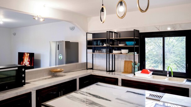 Una cocina moderna con encimera de mármol, electrodomésticos integrados y ventana con vistas a la vegetación.