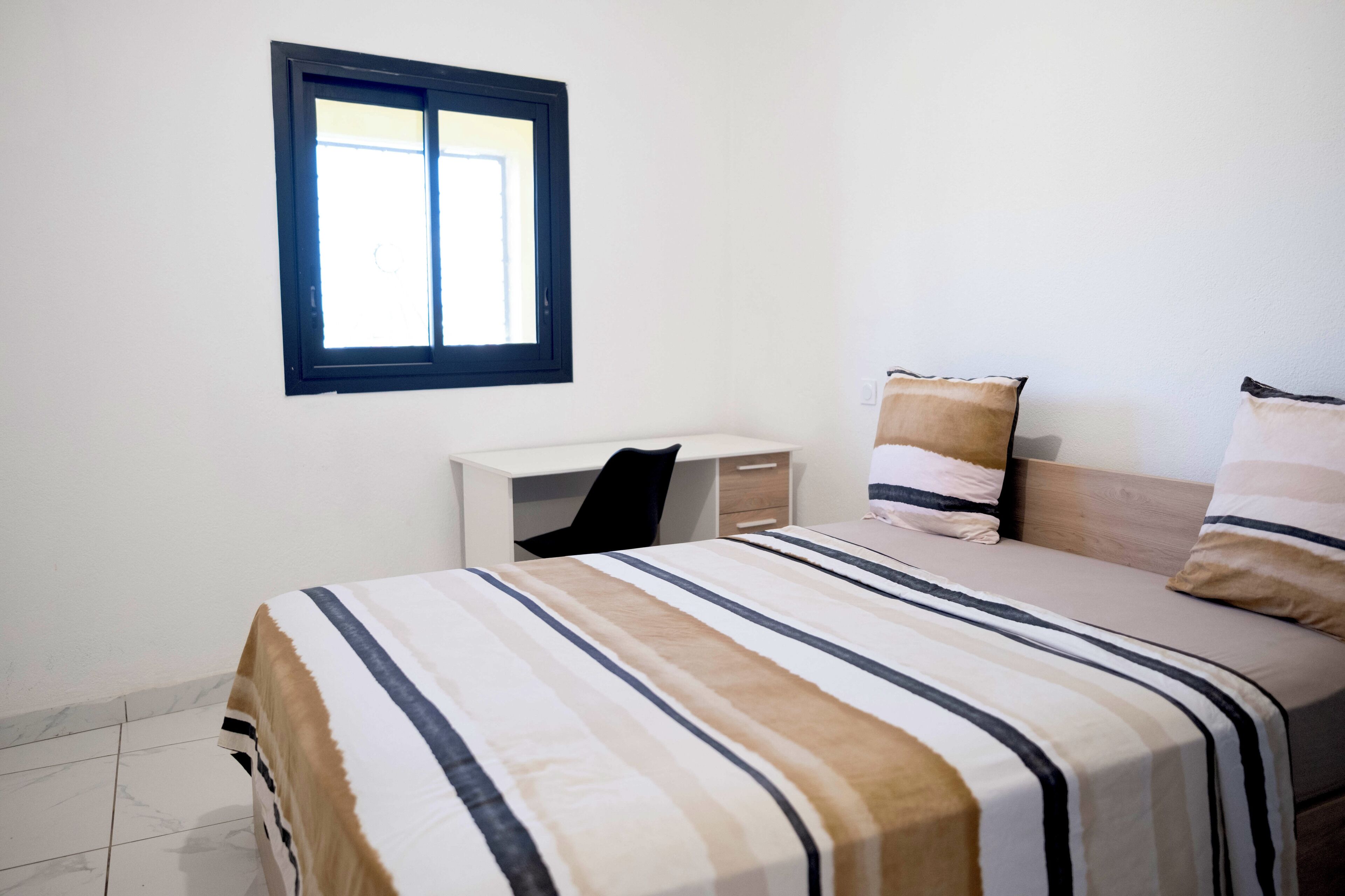 Una camera da letto con un letto, un comodino, una finestra e una sedia.