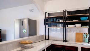 Una cocina moderna con refrigerador de acero inoxidable, encimeras de mármol y estantes empotrados con vajilla y copas.