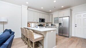 A modern kitchen with white cabinets, a stainless steel refrigerator, and a central island with bar stools. - Tiger’s Tail Trail 1245~Aubie's Reserve (Auburn)