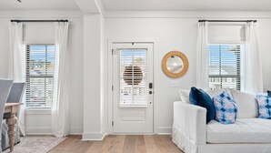 A clean, modern living room with a white door, a white sofa with patterned cushions, and a round mirror on the wall. - Tiger’s Tail Trail 1245~Aubie's Reserve (Auburn)