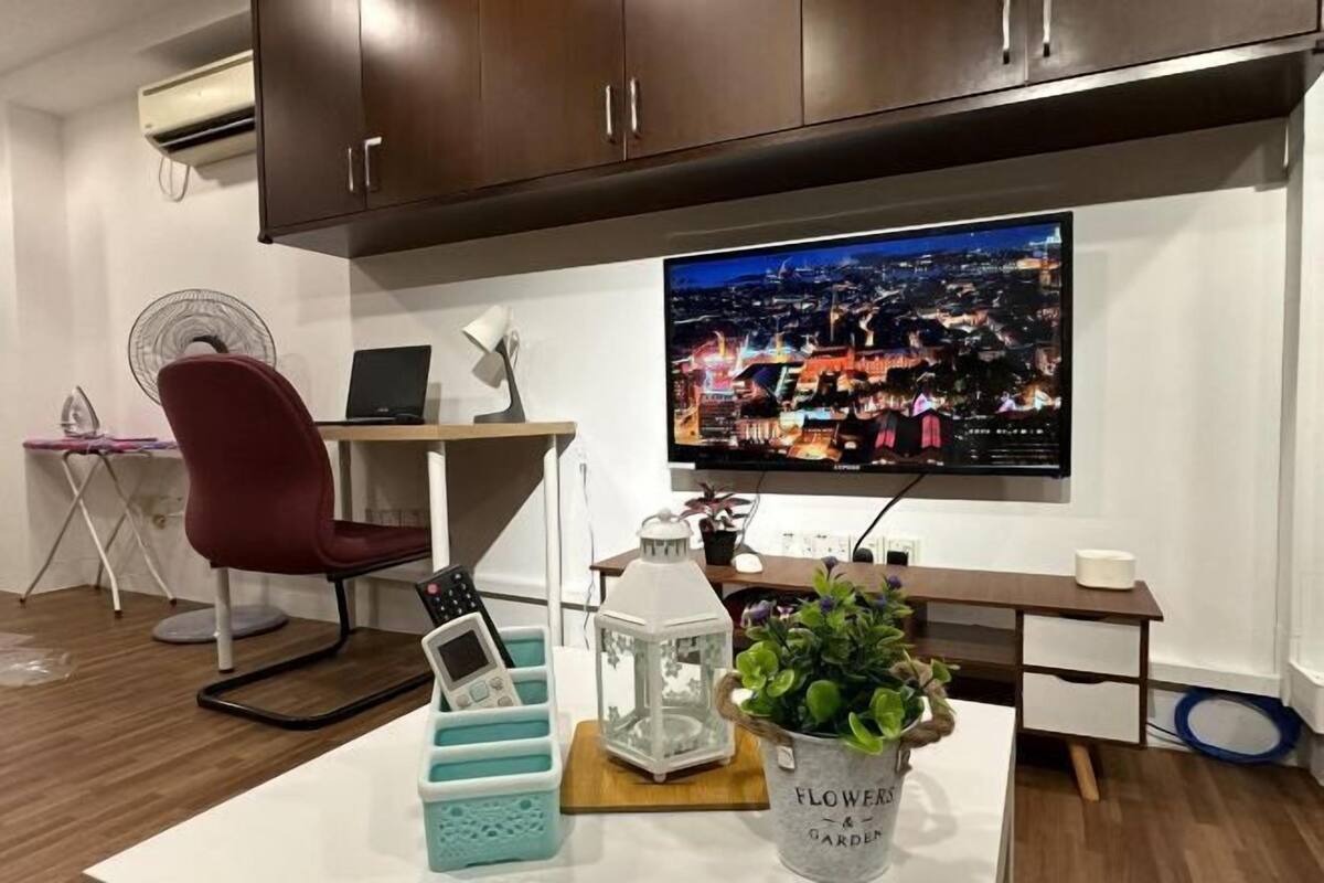 A modern room with a desk, chair, TV, air conditioner, and a potted plant.