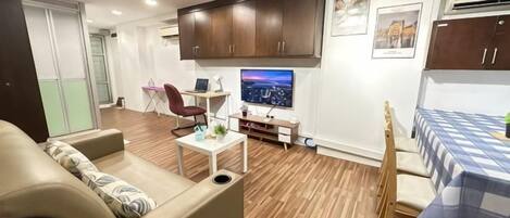 Een woonkamer met een bank, een eettafel met stoelen, een televisie en houten vloeren.