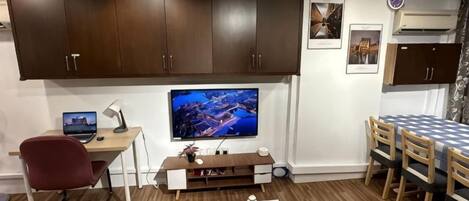 Una sala moderna con una televisión de pantalla plana, un escritorio con una computadora portátil, una mesa de comedor con sillas y un mueble grande.