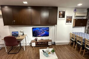 Una sala moderna con una televisión de pantalla plana, un escritorio con una computadora portátil, una mesa de comedor con sillas y un mueble grande.