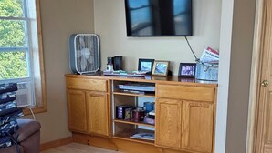 Un soggiorno con soffitto in legno, una televisione a parete, una ventola e un mobile contenitore con ripiani.