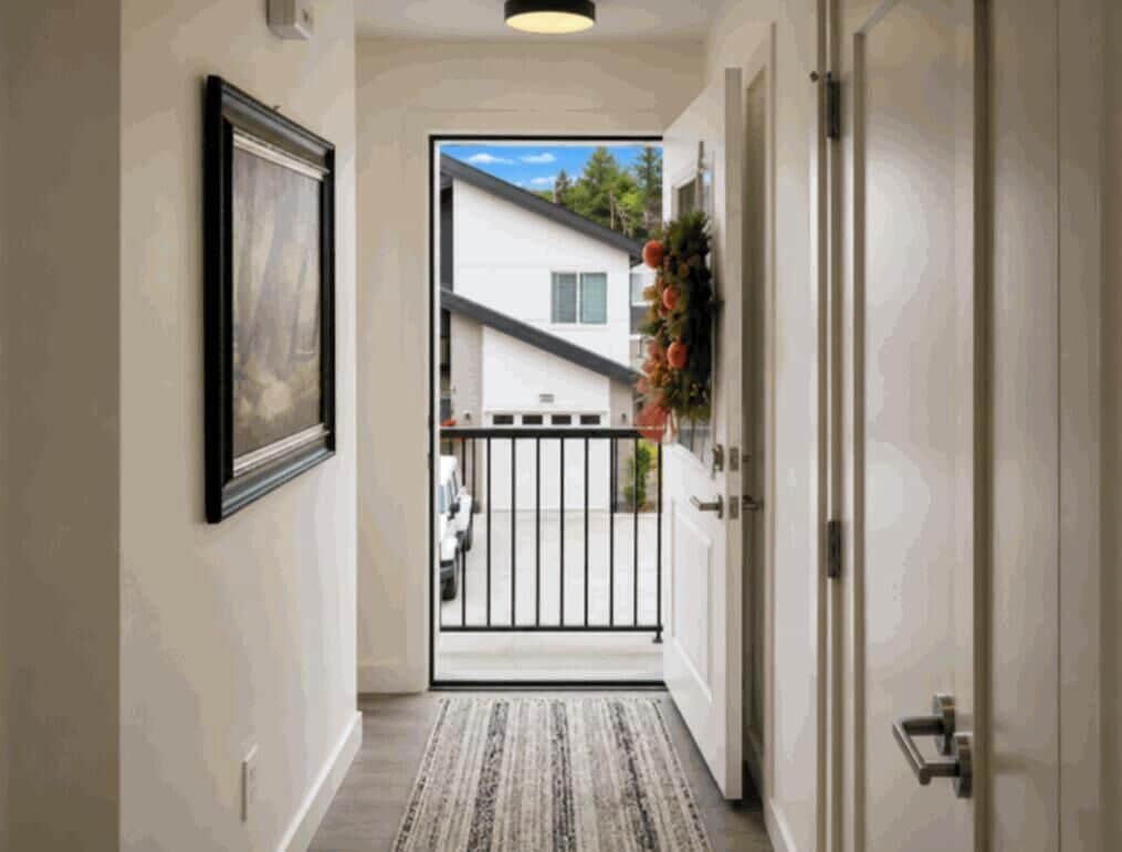 Un pasillo con un cuadro en la pared, una puerta a la derecha y vista de una casa a través de otra puerta abierta.