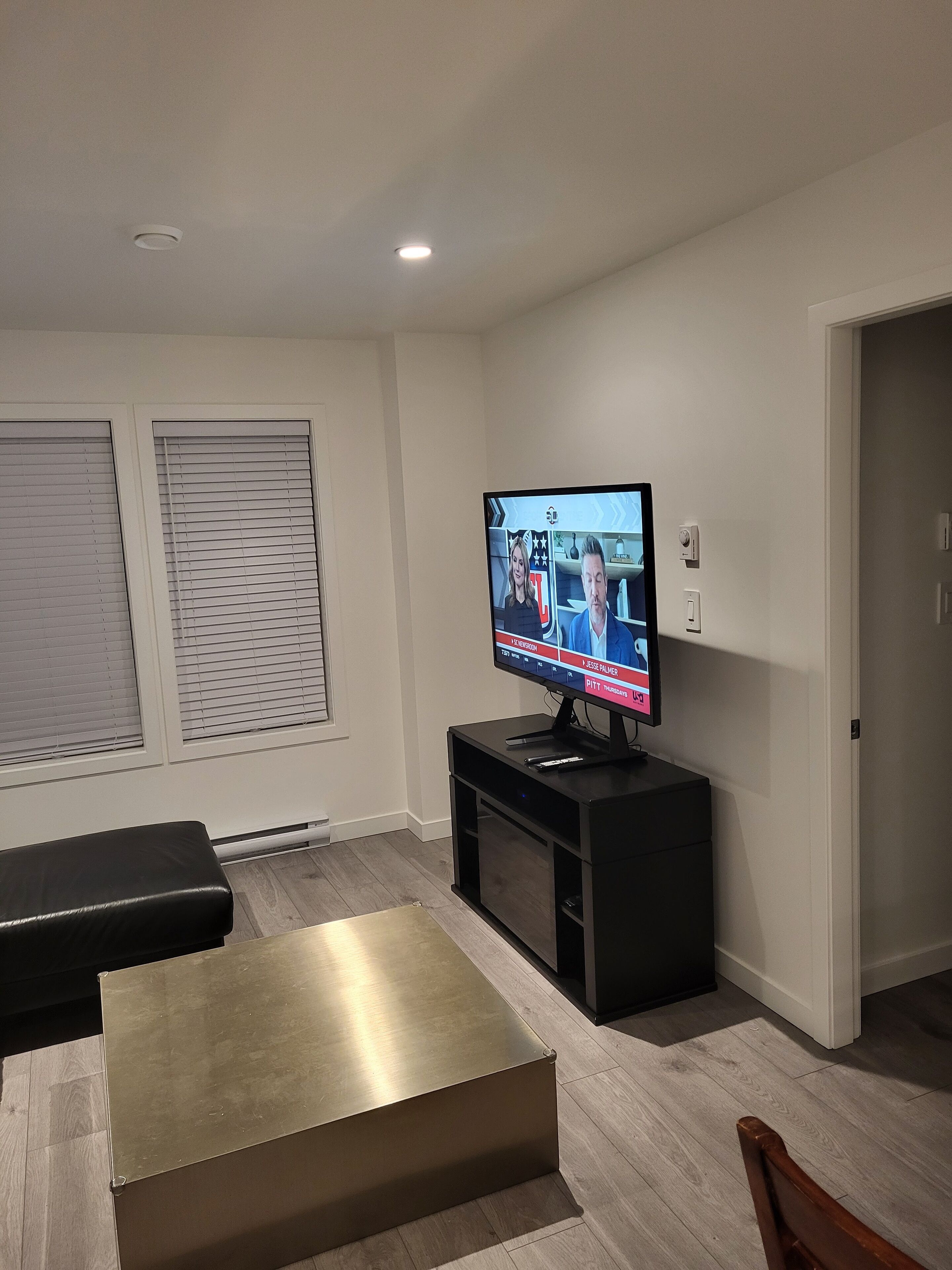 Una sala de estar moderna con un televisor de pantalla plana, un mueble de entretenimiento negro, un banco y una mesa de centro de madera.