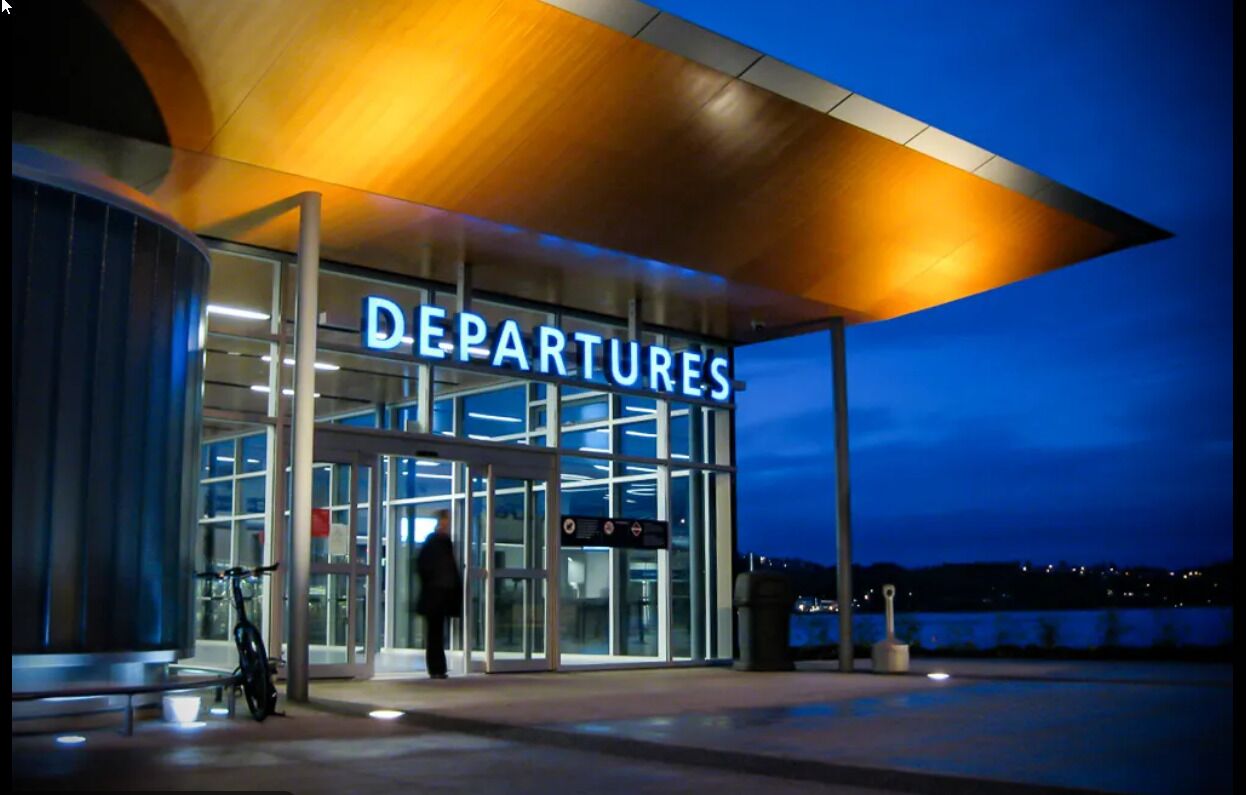 A modern building with a 'Departures' sign, glass doors, and a covered entrance area.