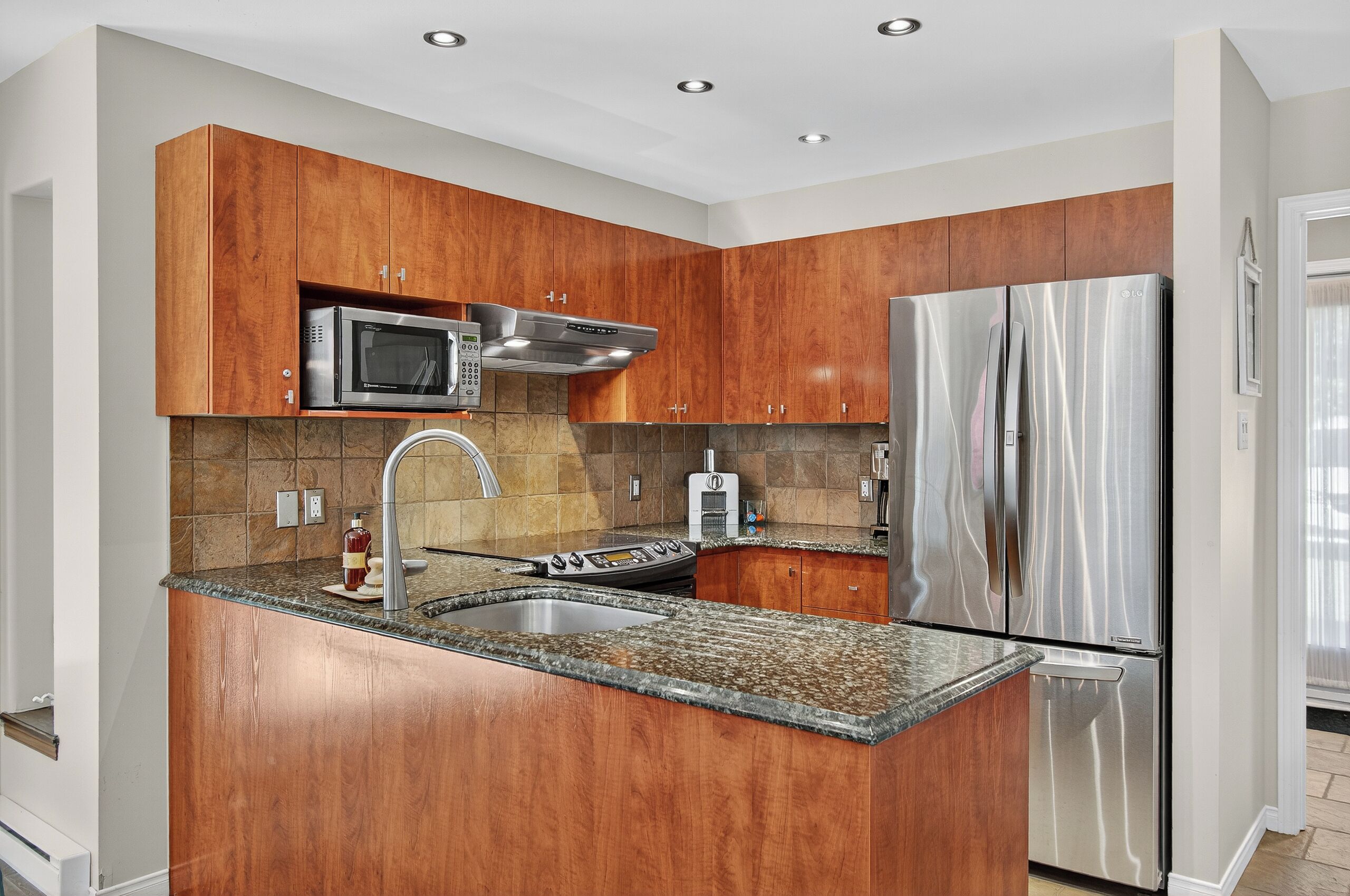 A modern kitchen with wooden cabinets, stainless steel appliances, and a granite countertop.