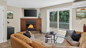 A living room with a fireplace, a sofa, a television, and a view of a deck. - 1704 Chemin du Golf (Mont-Tremblant)