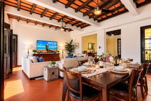 Un vaste salon doté d’un téléviseur diffusant l’émission « Puerto Rico Caribe », un coin repas aménagé pour un repas, et un espace salon confortable.