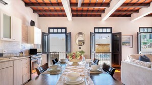 Un comedor con una larga mesa dispuesta para cuatro, una cocina contigua al espacio del comedor, y grandes ventanales que ofrecen vistas al exterior.