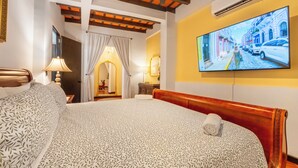 Habitación de hotel con una cama grande, un televisor en la pared y vista a una calle por la ventana.