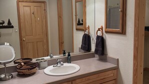 Ein Badezimmer mit einem Holzkosmetikschrank, einem runden Waschbecken, einem Spiegel und einem Handtuchhalter.