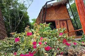 A wooden structure with a thatched roof, surrounded by lush greenery and pink flowers. - Asia Rainforest Resort (Semporna)