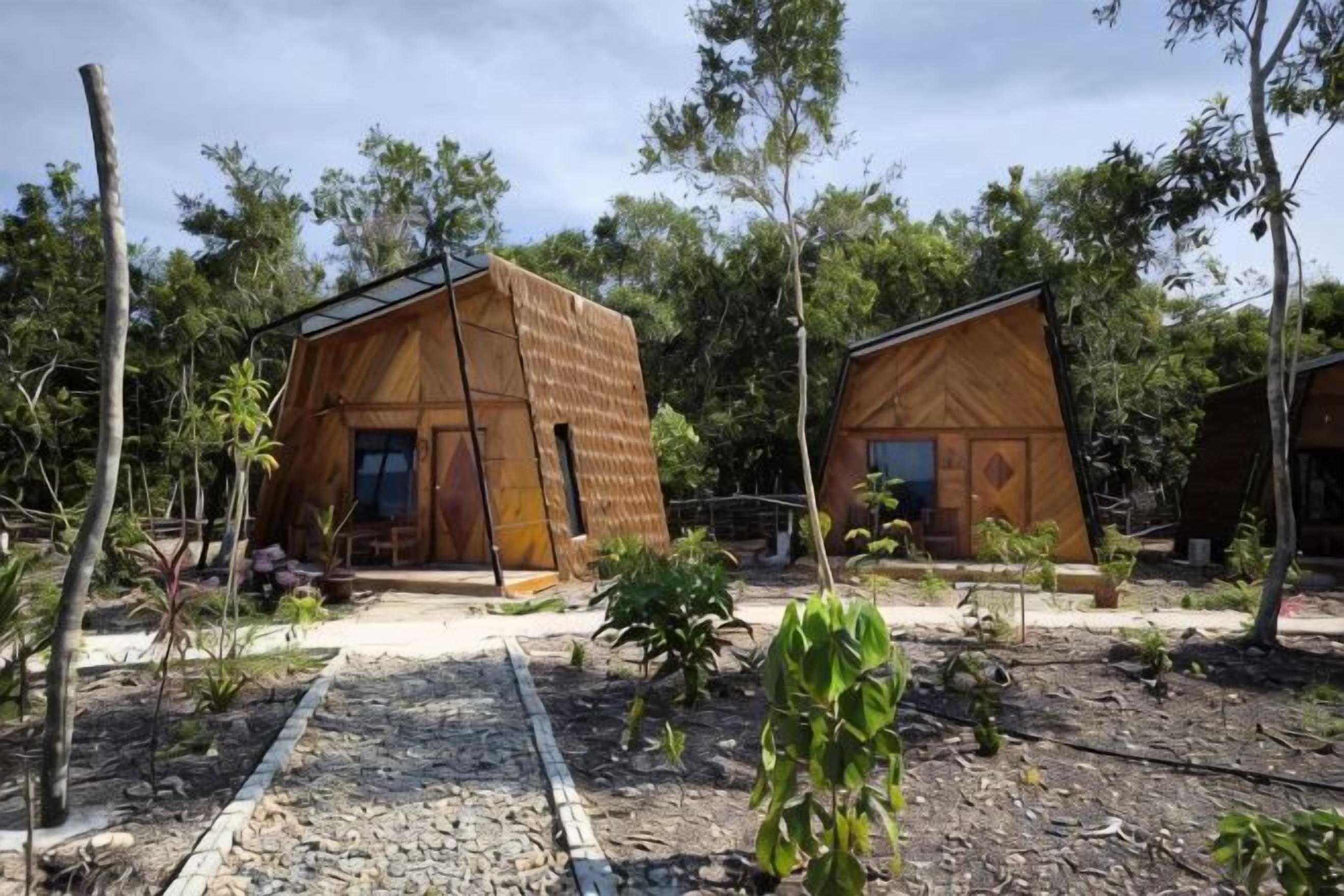 Two wooden cabins with a simple design, surrounded by trees and a gravel path.