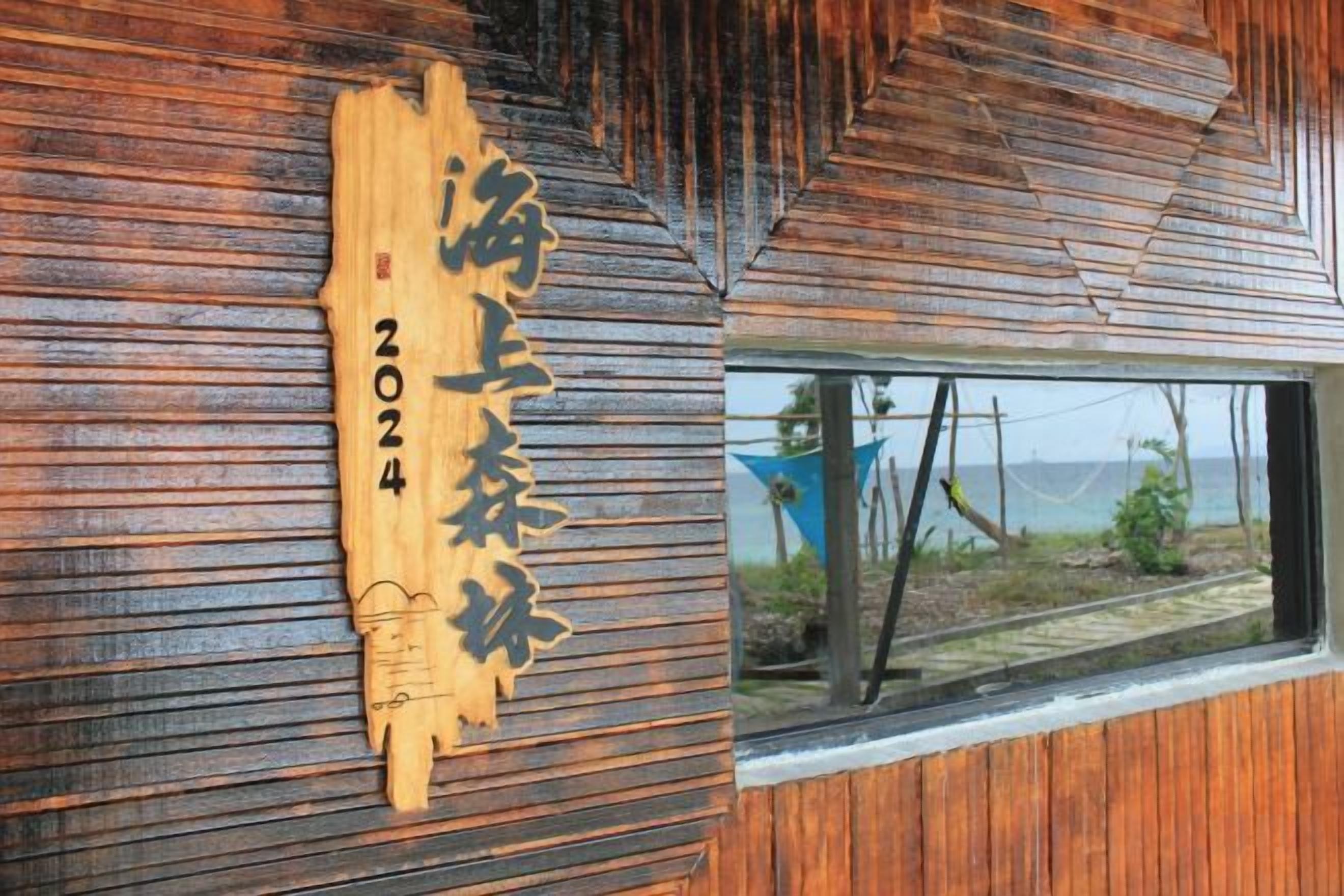 A wooden wall with a carved sign indicating '2024' and a window with a view of the sea.
