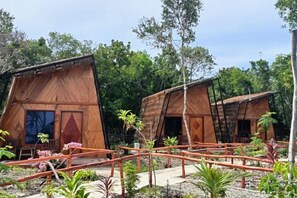 Two wooden cabins with thatched roofs, surrounded by a garden with various plants and a small bridge. - Asia Rainforest Resort (Semporna)