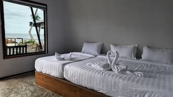 Ein Bett mit weißer Bettwäsche und zwei Schwänen auf den Kissen, ein Fenster mit Blick auf den Strand und ein hölzernes Kopfende.