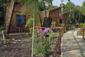 A rustic wooden cabin with a thatched roof, surrounded by a garden with purple flowers. - Asia Rainforest Resort (Semporna)