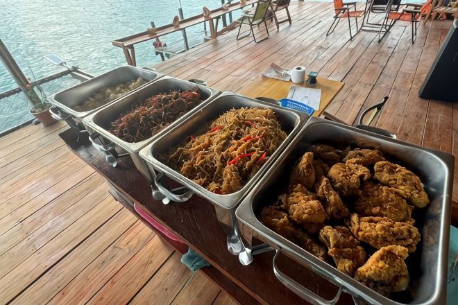 Ein Buffet mit verschiedenen Speisen auf einer Holzterrasse mit Blick aufs Wasser.