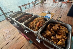 A buffet with various dishes on a wooden deck overlooking water. - Asia Rainforest Resort (Semporna)