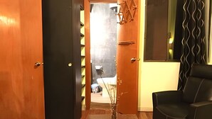 A room with a wooden floor, a black leather chair, and a door leading to a bathroom with a towel rack.