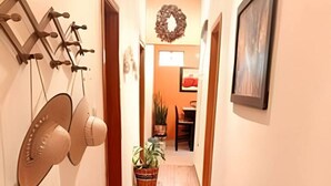 A narrow hallway with wooden flooring, a wall-mounted fan, a decorative wreath, and a potted plant.