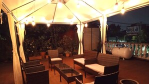 An outdoor patio area with wicker furniture, a glass table, and potted plants.