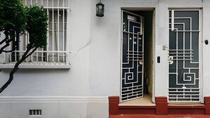 A white building with a window with white bars and a door with a geometric pattern.