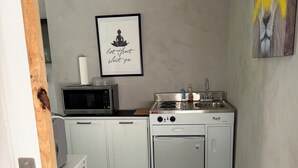 A compact kitchen with a microwave, stove, and sink. A framed picture hangs on the wall, and a vent is visible on the left. - Studio in vibrant Miami near the ports of Miami. (Miami)