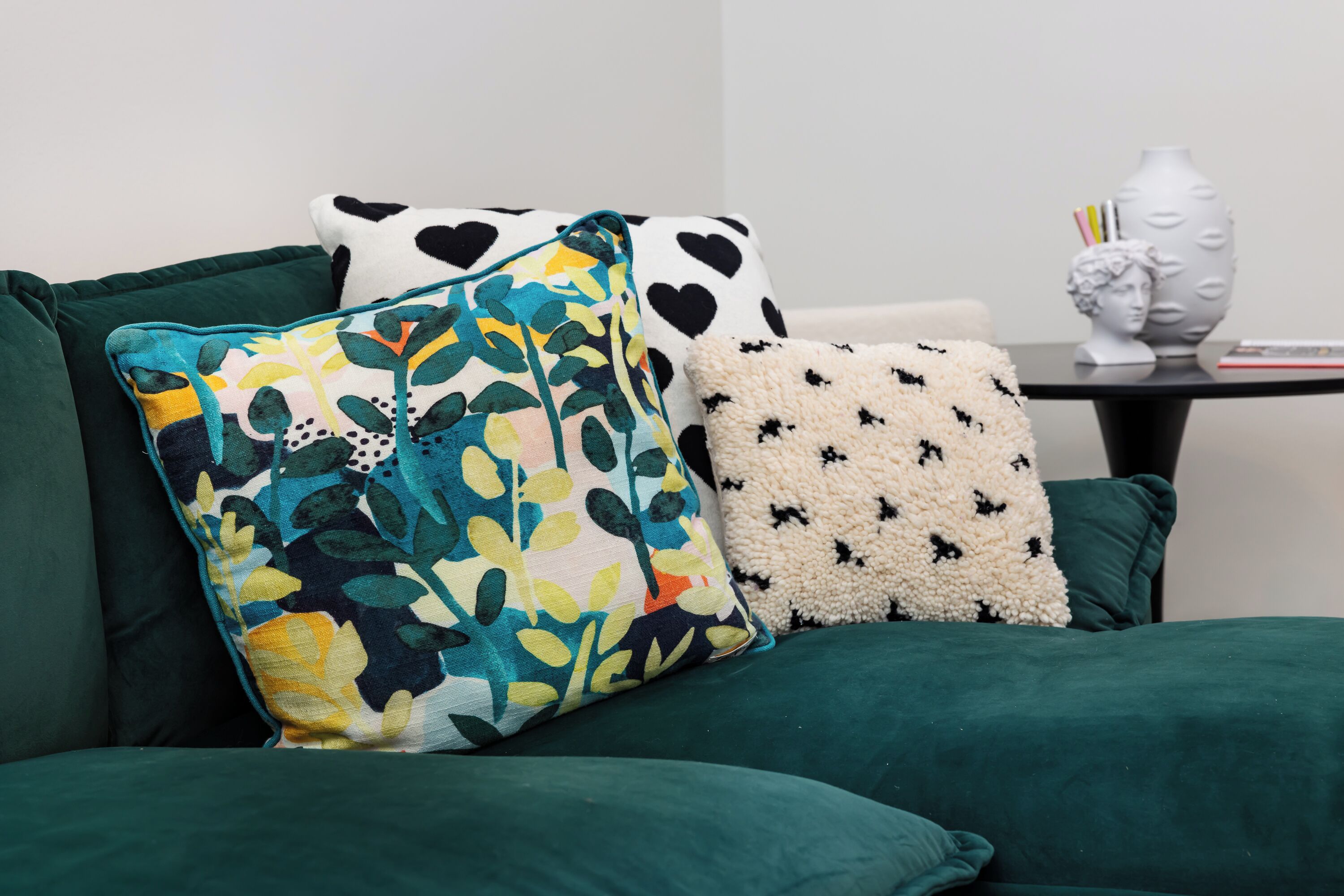 A green sofa with three decorative pillows in various patterns.