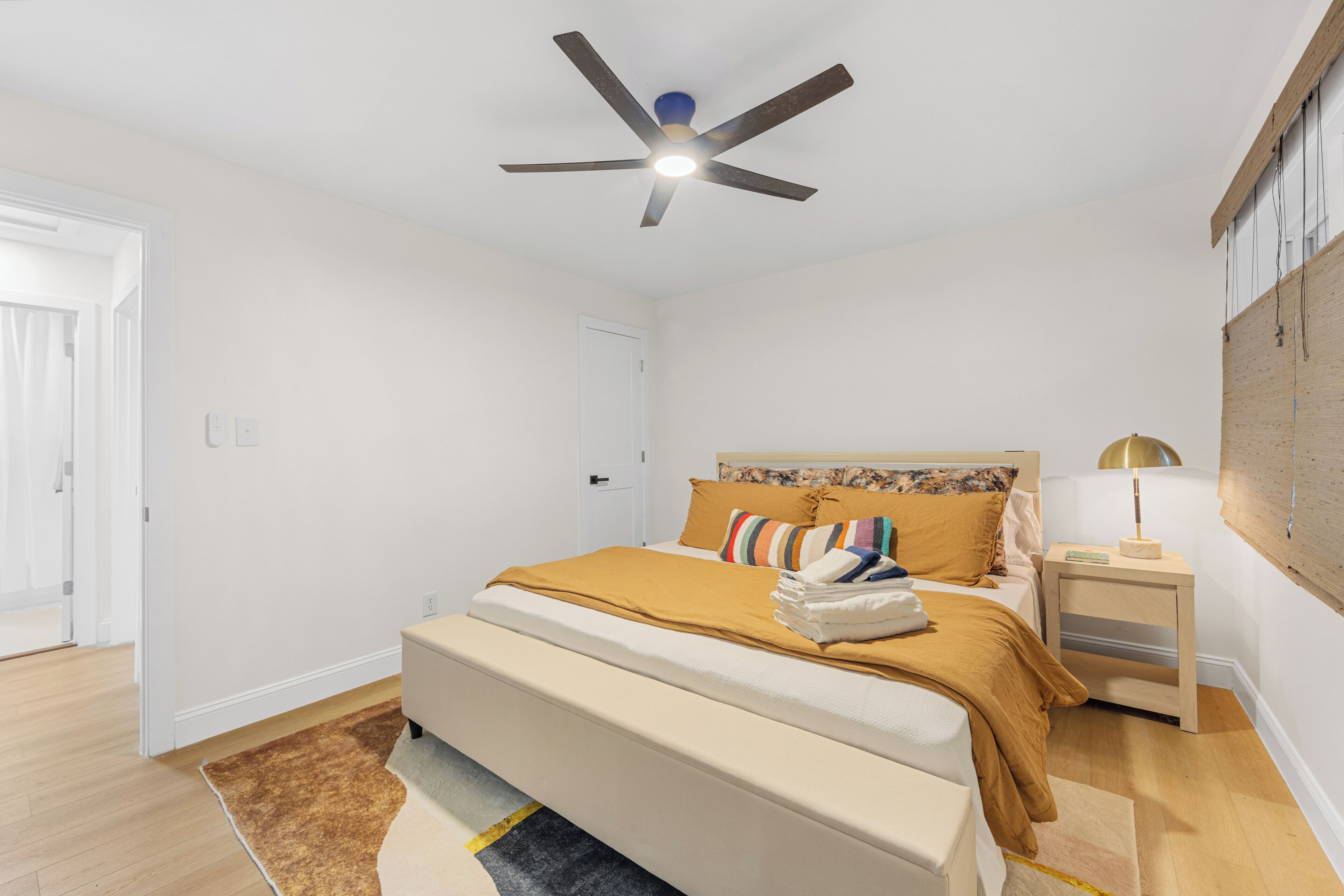 A bedroom with a bed, a ceiling fan, a nightstand, and a wall-mounted lamp.