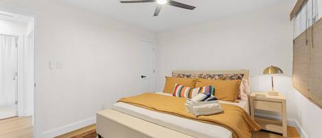 A bedroom with a bed, a ceiling fan, a nightstand, and a wall-mounted lamp.