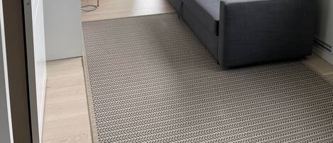 Un salon moderne avec un canapé gris, un tapis à motifs et une grande fenêtre.