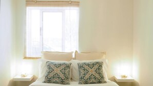Ein Schlafzimmer mit einem Bett, zwei Nachttischen, einem Fenster mit Jalousien und einer Pendelleuchte.