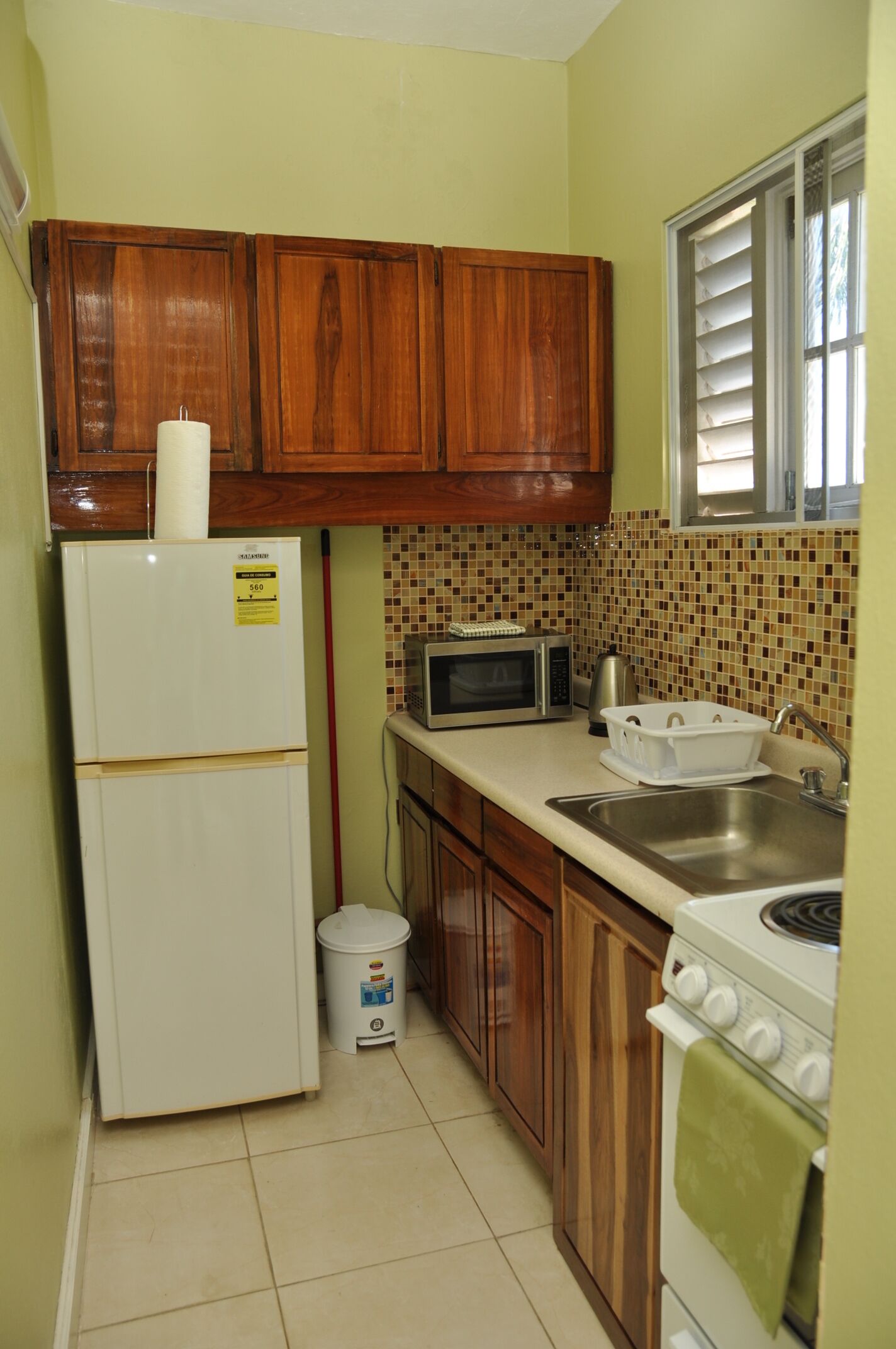 A compact kitchen with wooden cabinets, a refrigerator, a microwave, a sink, and a stove.
