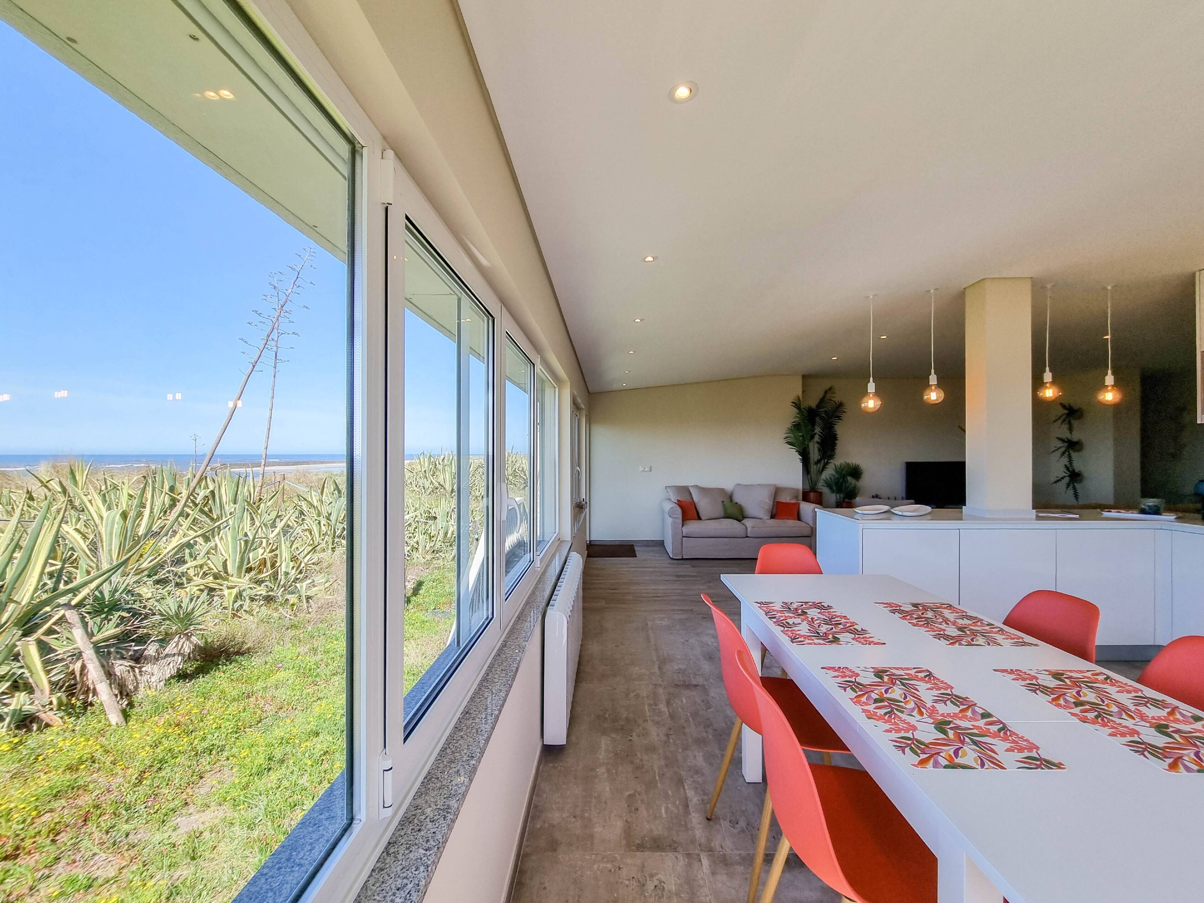 A modern dining area with a view of the ocean, a sofa, and a kitchen area with hanging lights.