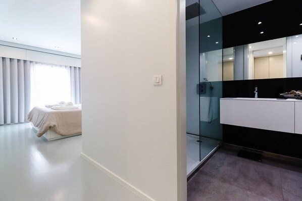 A modern bedroom with a bed, a large window with curtains, and a bathroom with a glass partition and a black countertop.